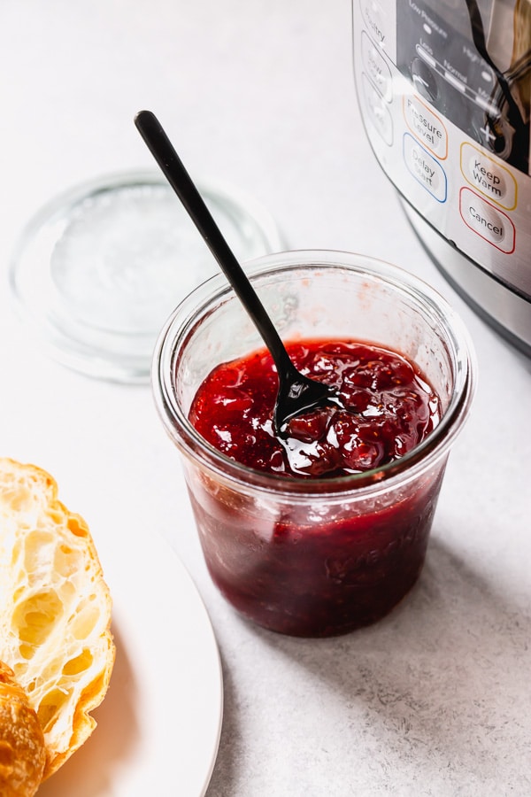 Red jam in a small glass pot.